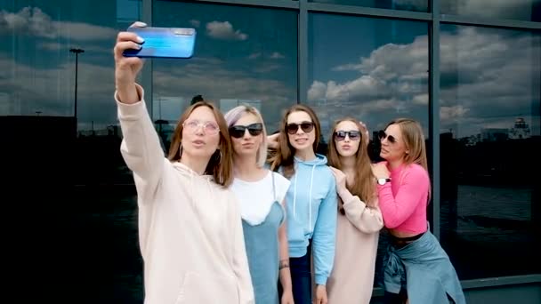 Hermosas chicas tomando una selfie al aire libre en la ciudad. Cinco novias en un smartphone cerca de ventanas de cristal. juventud, juventud. caminar en primavera. 20-25 años — Vídeo de stock