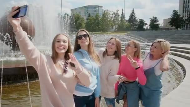 Selfie per strada in città. Cinque ragazze scattano foto su uno smartphone vicino alla fontana. giovani. fidanzate incontro concetto. Buona estate. fine settimana. 20-25 anni — Video Stock