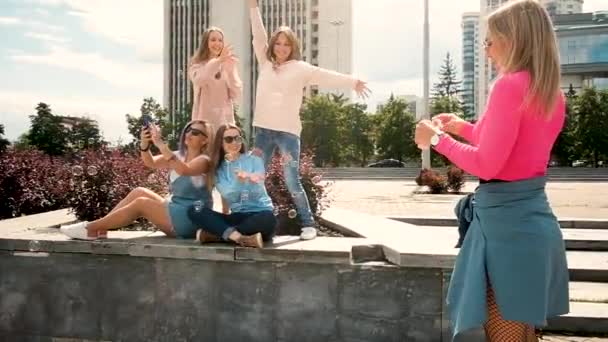 Jóvenes hermosas chicas soplan jabón en la ciudad. Fotografiado en un smartphone. Camina al aire libre. Cinco chicas de 20 a 25 años. El concepto de conocer novias. Divertirse y bromear — Vídeo de stock