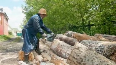 Elektrikli testereyle odun kesen bir adam. Ormanların tahrip edilmesi, ağaç kesme kavramı. Bir işçi ağaç keser ve talaşlar uçar. Yakacak odun yapıyorum. Sıkı çalışma kavramı. 60-65 yaşlarında yaşlı bir çiftçi.