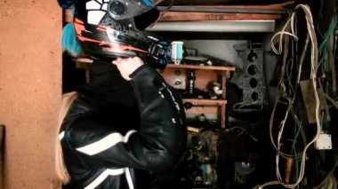 Güzel kadın motosikletçi garajda kask takıyor. Güvenlik kavramı, aktif bir yaşam tarzı, hız ve özgürlük. Moda motosiklet ekipmanları. 20-25 yaşlarında tatlı bir kız..