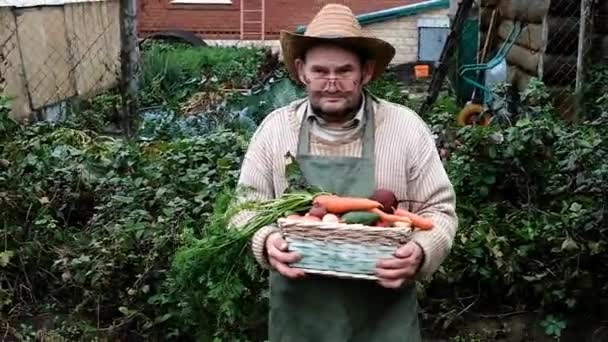 Farmář je postarší muž. nese košík se sklizní zeleniny. — Stock video