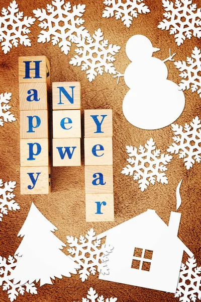 Happy New Year holiday image with a greeting text on wooden cubes and paper snowflakes and other festive shapes