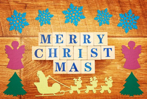 Text Merry Christmas on wooden background with festive bright colorful paper figures
