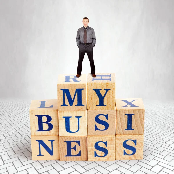 Self Confident adult Caucasian man stands on the top of heap of wooden blocks with a text My Business