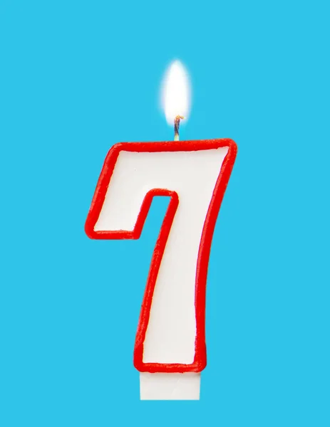 Burning wax candle for a birthday cake in the form of number seven