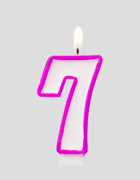 Burning wax candle for a birthday cake in the form of number seven