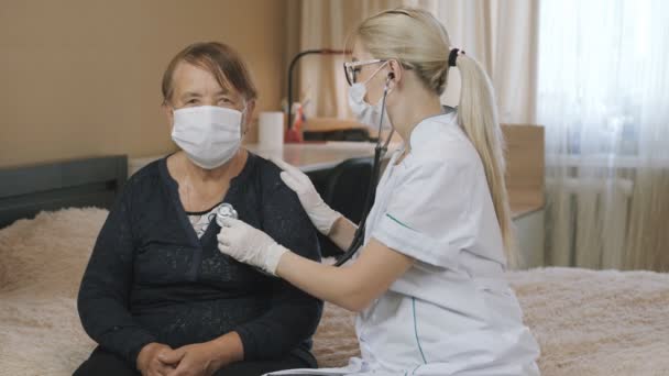 Doktor vyšetřuje starší ženu, domácí návštěva. Lékařská konzultace doma. Poslouchej stetoskopem.. — Stock video