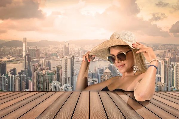 一个漂亮的金发姑娘 戴着太阳镜 头戴草帽 站在一座高楼大厦的顶楼 面对着一座现代化的城市 — 图库照片