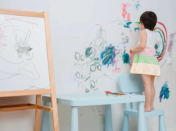 Uma menina, de 3 anos, pintou um olhar arqueado com tinta e um pincel na parede de seu quarto . — Fotografia de Stock