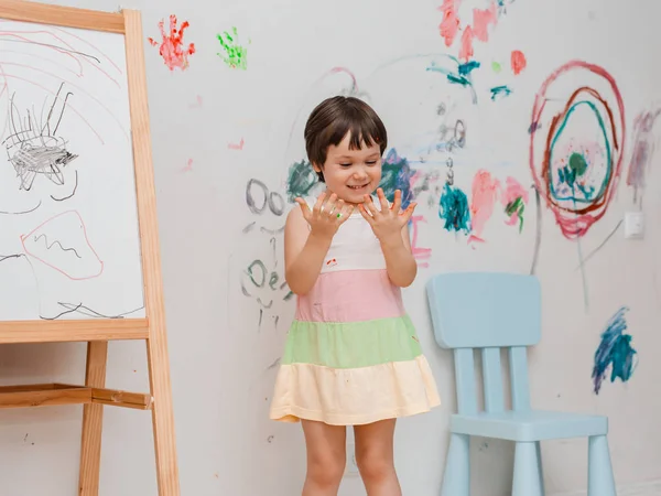 A little girl, 3 years old, painted an arched look with paint and a brush on the wall of her room.
