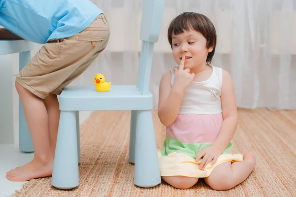 Schwester legt eine Gummiente auf einen Stuhl unter den Arsch ihrer Brüder und versteckt sich am Narrentag. — Stockfoto