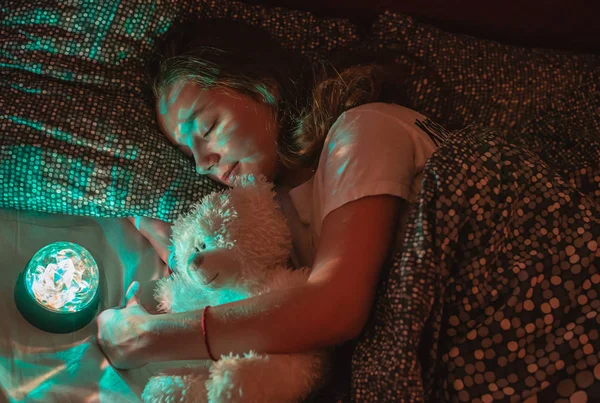 girl sleeps at night and sees quiet dreams. The teenager sleeps with a night radiant lamp in an embrace with a bear. The rest of the night. Healthy sleep.