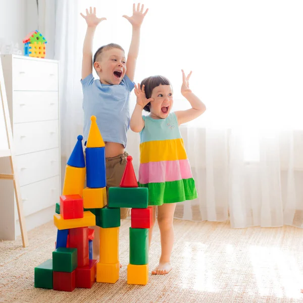 幸せな就学前の子供たちはおもちゃのブロックで遊ぶ 創造的な幼稚園の子供たちはプラスチックキューブの城を構築します 家族のための教育玩具 兄弟姉妹は部屋で遊ぶ — ストック写真