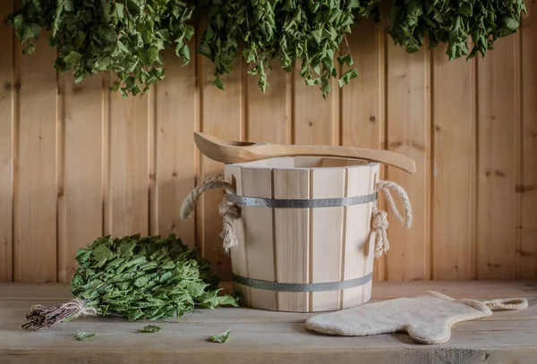 A wooden bucket and a birch broom in a Russian bath. Sauna. Free space on a wooden background.