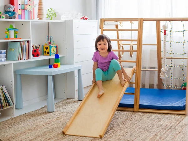 küçük kız ahşap bir ev sporları oyun kompleksi merdivenler, halkalar ve ip bir roller coaster sürme eğlenceli. Çocuk spor egzersizleri. Evde çocukların beden eğitimi.