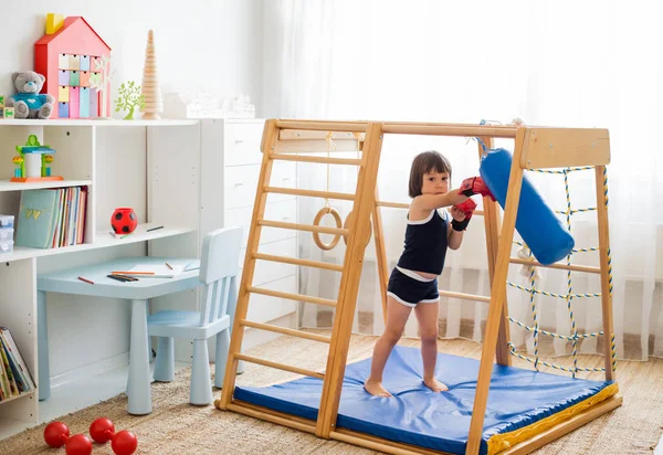 小さな子供は 木製のホームスポーツコンプレックスでボクシングに従事しています ボクシンググローブの女の子は梨を打ちます 子どもの身体発達 — ストック写真