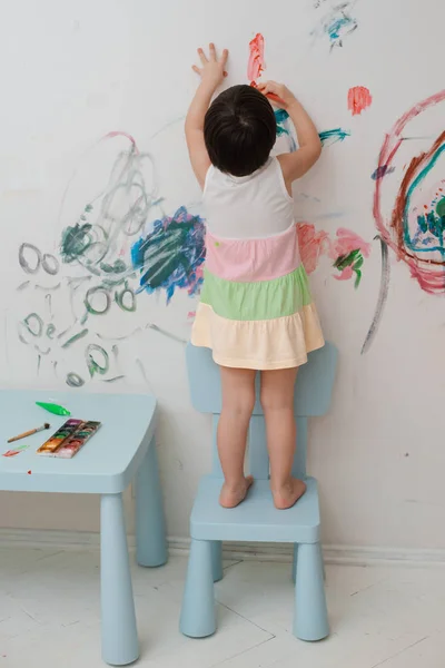 Uma menina, de 3 anos, pintou um olhar arqueado com tinta e um pincel na parede de seu quarto . — Fotografia de Stock