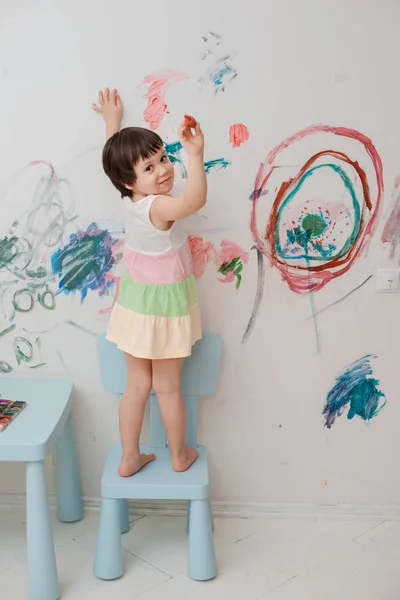 A little girl, 3 years old, painted an arched look with paint and a brush on the wall of her room.