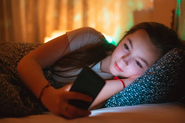 Chicas adolescentes tumbadas en la cama por la noche y usando un teléfono inteligente. Insomnio y el daño del teléfono inteligente antes de ir a la cama . — Foto de Stock