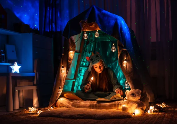 Ragazza adolescente sotto forma di anime seduto nella tenda della casa di gioco. Scenario con fantastica illuminazione ghirlanda . . Fotografia Stock