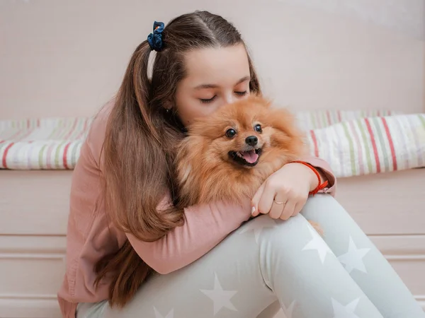 Adolescente con una raza de perro Spitz se regocija con una mascota en casa en el suelo . —  Fotos de Stock