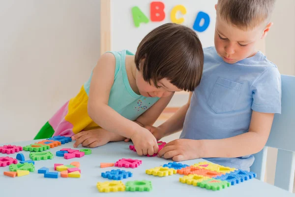 Um menino e uma menina coletam um quebra-cabeça suave na mesa. Irmão e irmã se divertir jogando juntos no quarto. — Fotografia de Stock