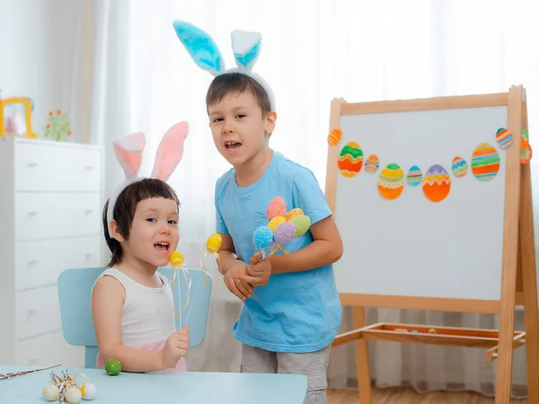 Mały chłopiec i dziewczynka w uszy królika są gry z pisanki. Dzieci z okazji Wielkanocy. — Zdjęcie stockowe