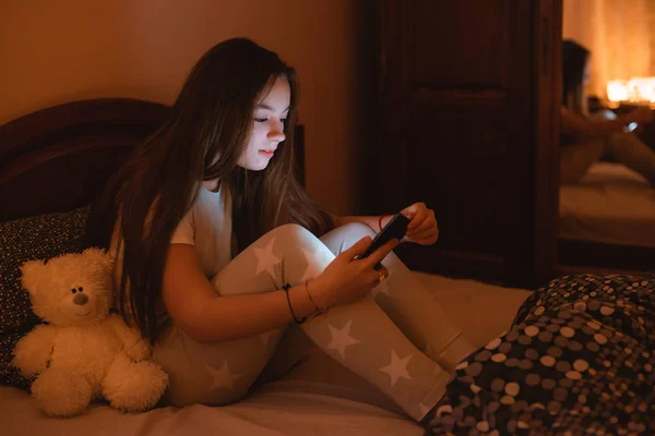 Chicas adolescentes tumbadas en la cama por la noche y usando un teléfono inteligente. Insomnio y el daño del teléfono inteligente antes de ir a la cama . — Foto de Stock
