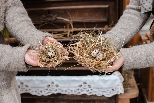 Nidi decorativi di paglia con uovo di quaglia primo piano in mani femminili su sfondo rustico vintage . — Foto Stock