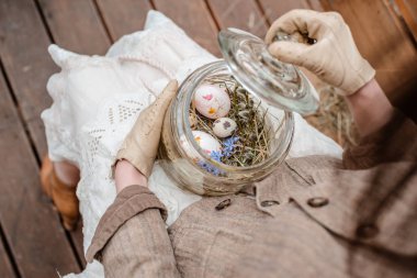 Bir cam kavanozda Dekoratif Paskalya yumurtaları yakın çekim dizlerinin üzerinde ve vintage giysiler içinde bir kızın elinde.