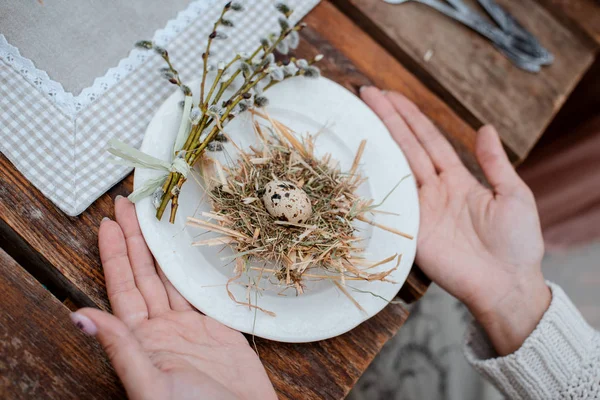 Nids de paille décoratifs avec oeuf de caille en gros plan dans les mains des femmes sur fond rustique vintage . — Photo