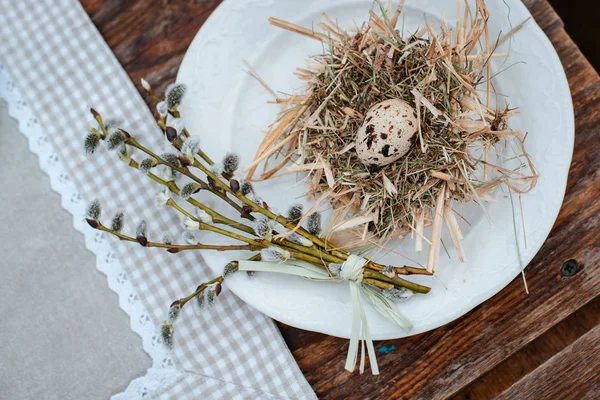 Nid décoratif de paille sur une assiette avec oeuf de caille de Pâques sur une table de jardin de fête servie à l'extérieur. Ferme. Style rustique . — Photo