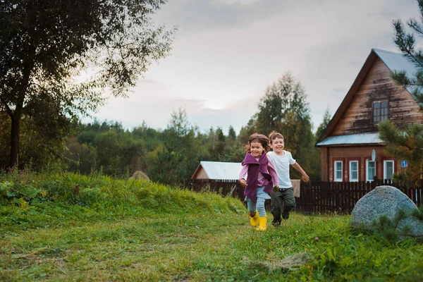 Bruder und Schwester führen im Hintergrund des Dorfhauses Hand in Hand. Urlaub im Dorf mit meiner Großmutter. — Stockfoto