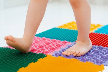 Bebek ayak masajı minderinde yeni yürümeye başlayan çocuk. Ortopedik masaj halısı üzerinde bacak egzersizleri. Düz taban ve halluks valgus önleme