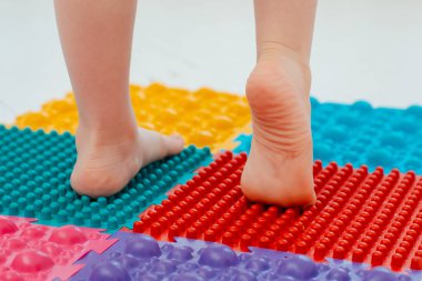 Bebek ayak masajı minderinde yeni yürümeye başlayan çocuk. Ortopedik masaj halısı üzerinde bacak egzersizleri. Düz taban ve halluks valgus önleme
