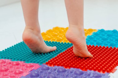 Bebek ayak masajı minderinde yeni yürümeye başlayan çocuk. Ortopedik masaj halısı üzerinde bacak egzersizleri. Düz taban ve halluks valgus önleme