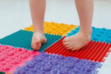 Bebek ayak masajı minderinde yeni yürümeye başlayan çocuk. Ortopedik masaj halısı üzerinde bacak egzersizleri. Düz taban ve halluks valgus önleme