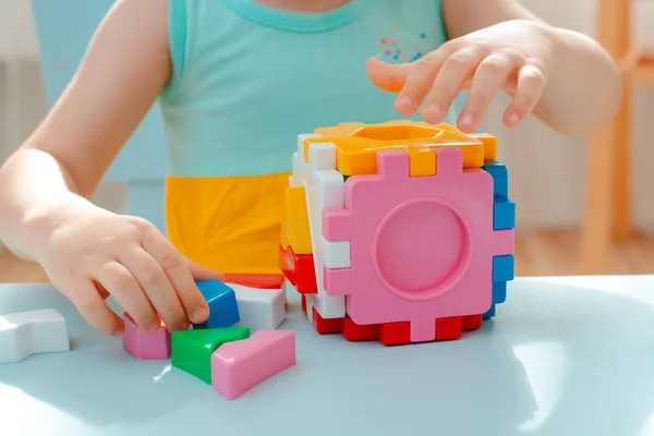 Close-up das mãos da criança coletar classificador de quebra-cabeça. Cubo com formas geométricas inseridas e blocos de plástico colorido . — Fotografia de Stock