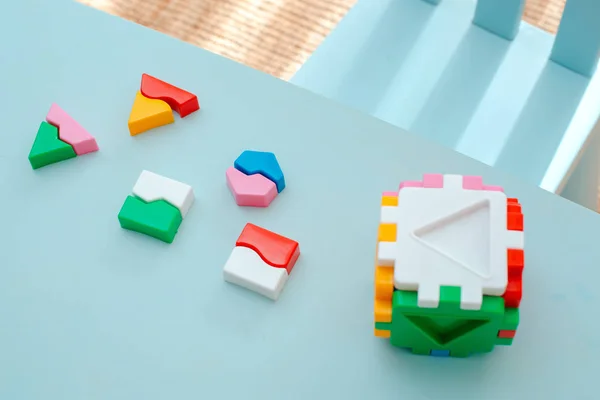 Nahaufnahme der Hände des Kindes sammeln Puzzle-Sortierer. Würfel mit eingefügten geometrischen Formen und farbigen Kunststoffblöcken. — Stockfoto