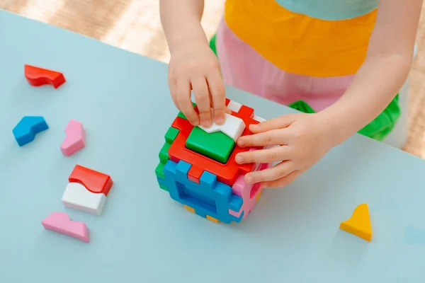 Close-up of the child's hands collect puzzle sorter. Cube with inserted geometric shapes and colored plastic blocks. — Stock Photo, Image