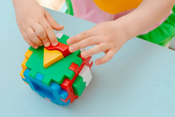 Gros plan des mains de l'enfant collecter puzzle trieur. Cube avec des formes géométriques insérées et des blocs en plastique coloré. — Photo