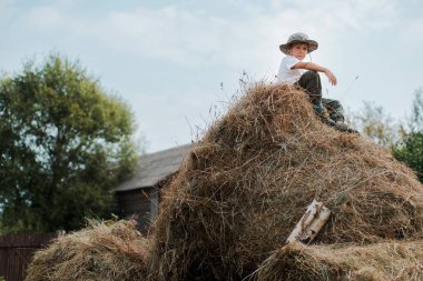 küçük çocuk köyde büyük bir samanlık yükseklikte oturuyor. Çocuk çiftçi.