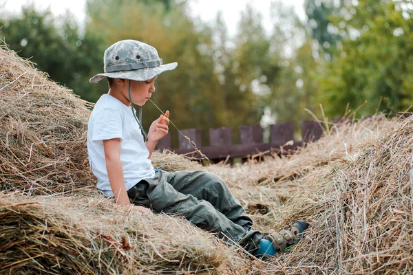 Kleiner Junge, der auf der Höhe eines großen Heuhaufens im Dorf sitzt. das Kind der Bauer. — Stockfoto