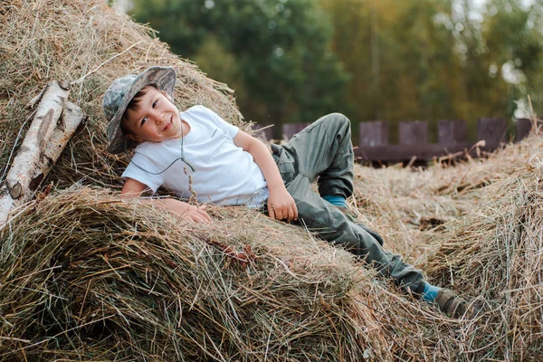 Kleiner Junge, der auf der Höhe eines großen Heuhaufens im Dorf sitzt. das Kind der Bauer. — Stockfoto