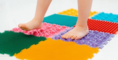Bebek ayak masajı minderinde yeni yürümeye başlayan çocuk. Ortopedik masaj halısı üzerinde bacak egzersizleri. Düz taban ve halluks valgus önleme