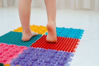 Bebek ayak masajı minderinde yeni yürümeye başlayan çocuk. Ortopedik masaj halısı üzerinde bacak egzersizleri. Düz taban ve halluks valgus önleme