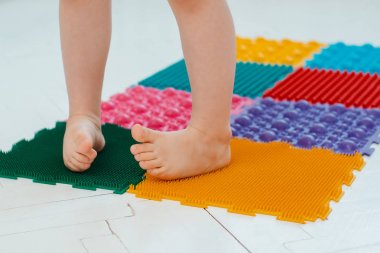 Bebek ayak masajı minderinde yeni yürümeye başlayan çocuk. Ortopedik masaj halısı üzerinde bacak egzersizleri. Düz taban ve halluks valgus önleme