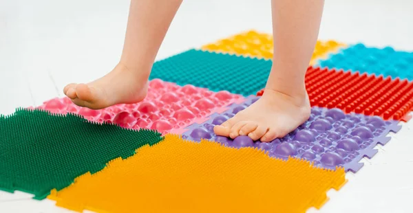 Toddler on baby foot massage mat. Exercises for legs on orthopedic massage carpet. prevention of flat feet and hallux valgus — Stock Photo, Image