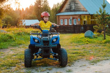 küçük çocuk 5 yıl çocuk Atv sürmek yaz tatilinde güneş batan arka plan köy evi. quadbike